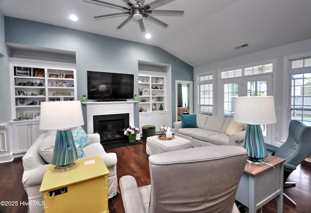 4875 Frasier Cir, Shallotte, NC 28470 - living room featuring a ceiling fan, vaulted ceiling, dark wood-style flooring, a fireplace with flush hearth, and built in shelves