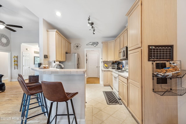 820 Jackeys Creek Ln SE, Leland, NC 28451 - kitchen featuring appliances with stainless steel finishes, light brown cabinets, a kitchen bar, tile countertops, and ceiling fan