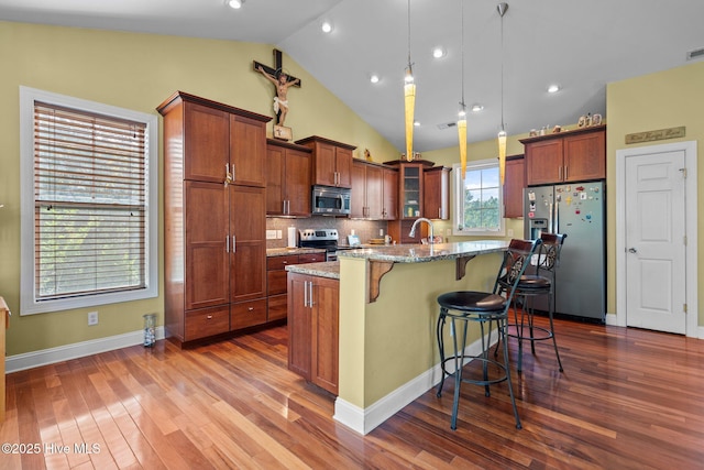 9406 Voyagers Way, Wilmington, NC 28412 - kitchen featuring stainless steel appliances, a breakfast bar, light stone countertops, vaulted ceiling, and a center island with sink