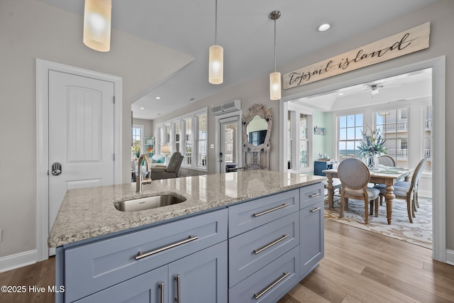 4340 Island Dr, North Topsail Beach, NC 28460 - kitchen featuring open floor plan, an island with sink, light stone counters, wood finished floors, and hanging light fixtures