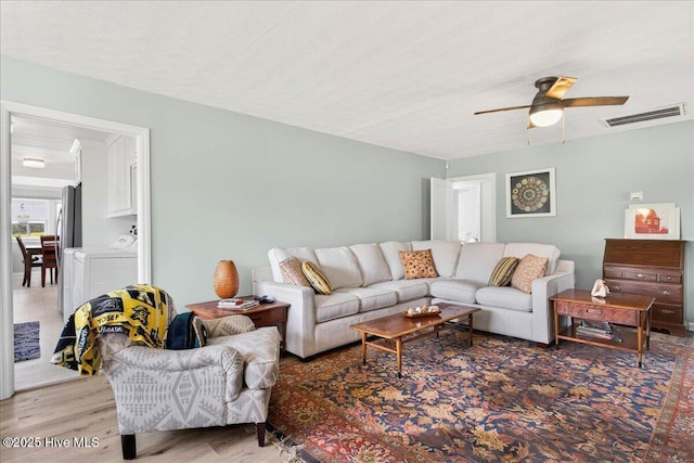 living area featuring light wood-style flooring, a ceiling fan, and washing machine and dryer