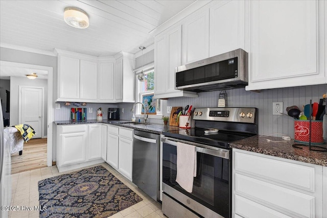 kitchen with stainless steel appliances, white cabinets, dark stone counters, ornamental molding, and light tile patterned floors