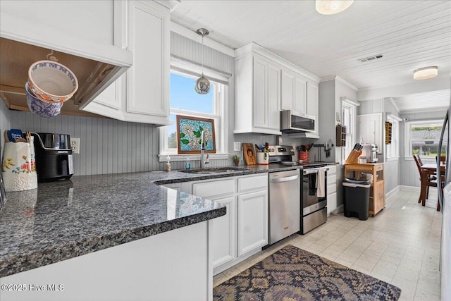 kitchen featuring appliances with stainless steel finishes, white cabinetry, dark stone counters, and decorative light fixtures