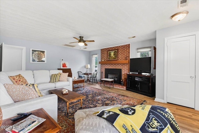 living area with plenty of natural light, wood finished floors, a ceiling fan, and a brick fireplace