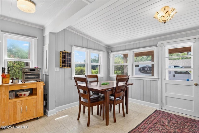 dining room with crown molding, light flooring, wooden walls, and a wooden ceiling with exposed beams