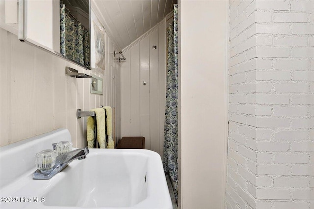 full bathroom featuring a shower with curtain and brick wall
