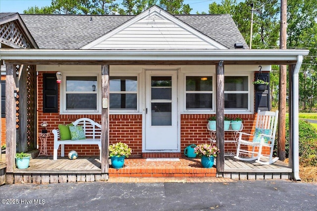 view of front of house featuring brick siding, roof with shingles, and a porch