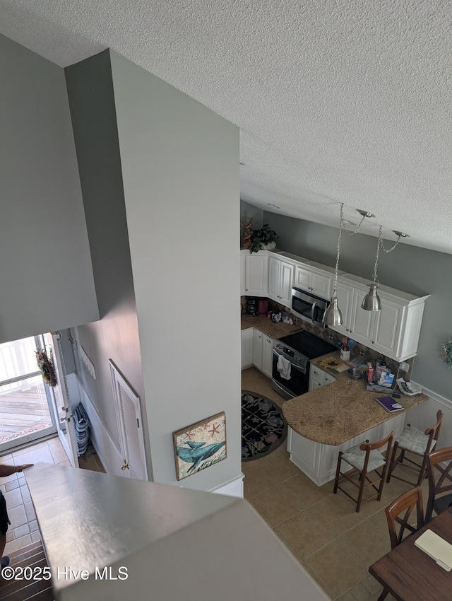 7 Oleander Ln, Ocean Isle Beach, NC 28469 - kitchen featuring stainless steel appliances, light tile patterned flooring, a textured ceiling, white cabinets, and a peninsula