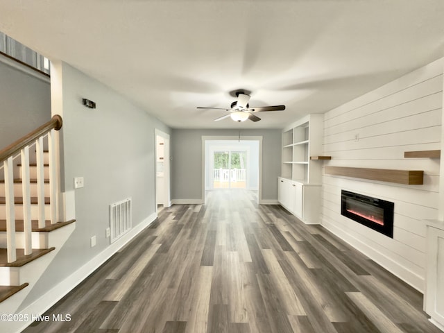 9891 Red Fox, Winnabow, NC 28479 - unfurnished living room featuring stairway, ceiling fan, a glass covered fireplace, and dark wood-style flooring