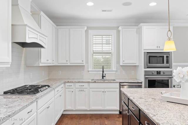 9385 Fallen Pear Ln NE, Leland, NC 28451 - kitchen with appliances with stainless steel finishes, custom range hood, white cabinets, tasteful backsplash, and ornamental molding