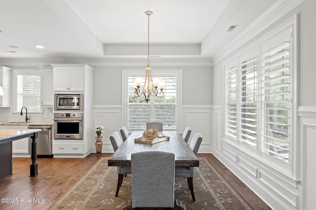9385 Fallen Pear Ln NE, Leland, NC 28451 - dining space with dark wood finished floors, a decorative wall, a chandelier, a wainscoted wall, and a tray ceiling