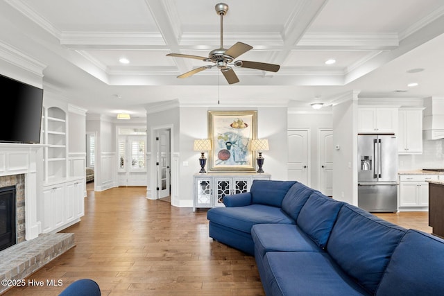 9385 Fallen Pear Ln NE, Leland, NC 28451 - living room with ceiling fan, coffered ceiling, a glass covered fireplace, crown molding, and light wood-style flooring