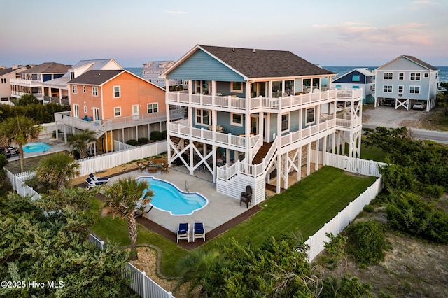 6626 W Beach Dr, Oak Island, NC 28465 - back of property at dusk with a fenced backyard, stairs, a patio, a balcony, and roof with shingles
