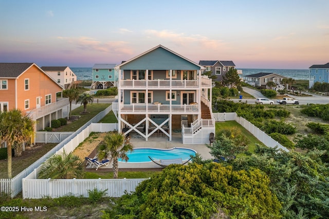 6626 W Beach Dr, Oak Island, NC 28465 - back of house at dusk featuring stairs, a fenced backyard, and a balcony