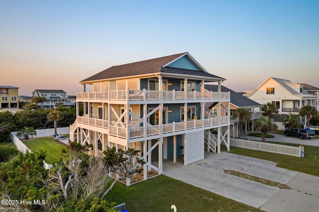 6626 W Beach Dr, Oak Island, NC 28465 - back of property at dusk with concrete driveway, a shingled roof, a balcony, and a carport