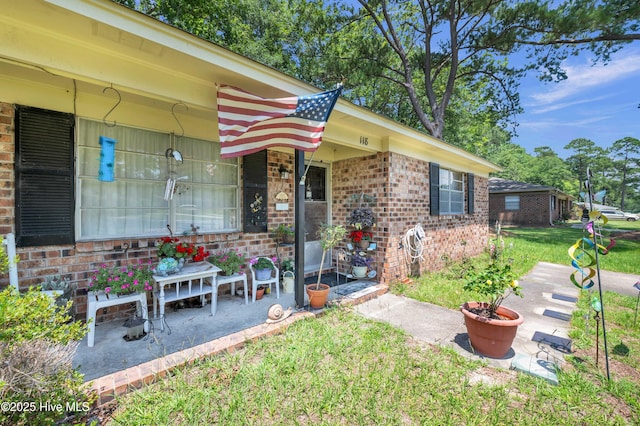 doorway to property with brick siding, a lawn, and a patio