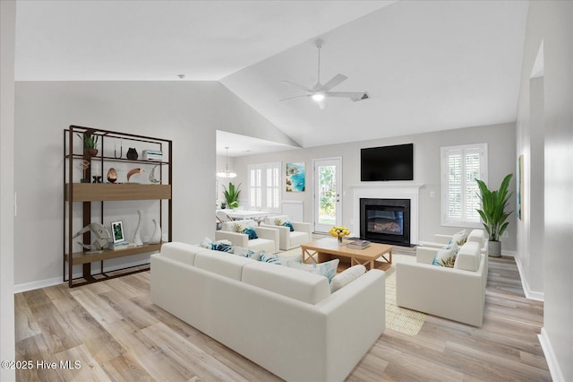 111 Yaupon Ct, Hampstead, NC 28443 - living room featuring light wood-style floors, a glass covered fireplace, vaulted ceiling, ceiling fan, and a chandelier