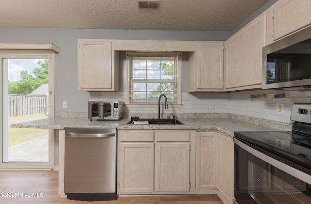 6723 Newbury Way, Wilmington, NC 28411 - kitchen with stainless steel appliances, light brown cabinetry, decorative backsplash, and a textured ceiling