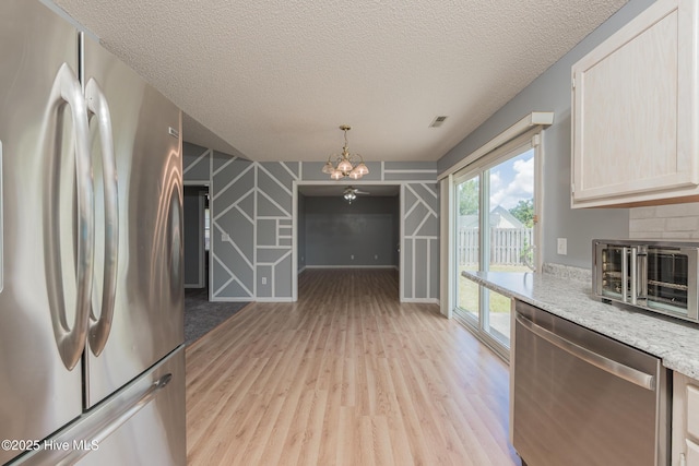 6723 Newbury Way, Wilmington, NC 28411 - kitchen featuring appliances with stainless steel finishes, a chandelier, light wood finished floors, a textured ceiling, and light stone counters