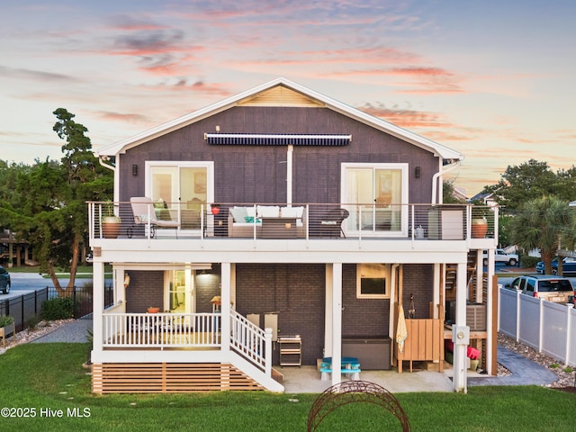 15 Coral Dr, Wrightsville Beach, NC 28480 - back of house at dusk with a balcony, a fenced backyard, a patio, and brick siding