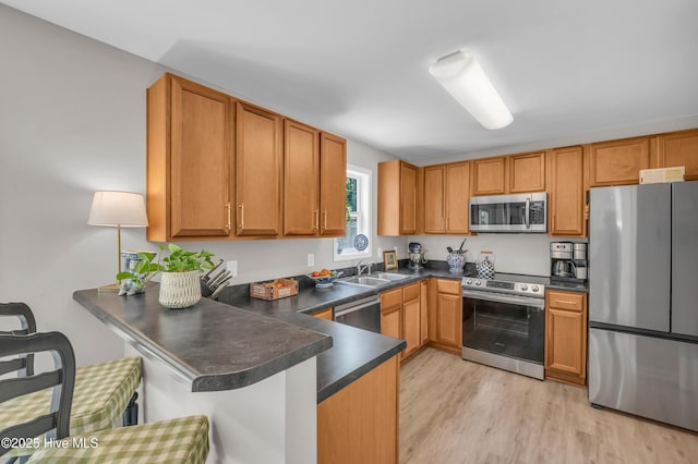 3239 Kellerton Pl, Wilmington, NC 28409 - kitchen featuring stainless steel appliances, dark countertops, a peninsula, light wood-style floors, and a kitchen breakfast bar
