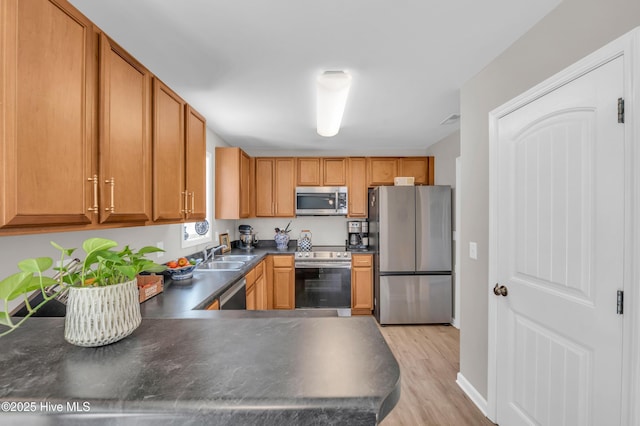3239 Kellerton Pl, Wilmington, NC 28409 - kitchen featuring stainless steel appliances, dark countertops, light wood finished floors, brown cabinets, and a peninsula