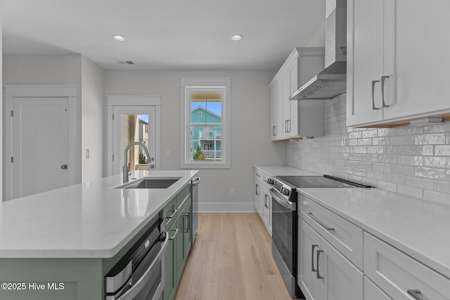 207 Spartanburg Ave Unit 1 & 2, Carolina Beach, NC 28428 - kitchen with wall chimney range hood, appliances with stainless steel finishes, light wood-type flooring, decorative backsplash, and a kitchen island with sink