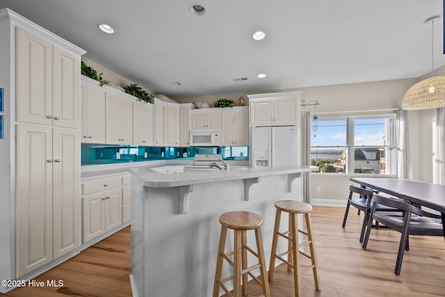 8202 5th Ave, North Topsail Beach, NC 28460 - kitchen featuring white appliances, light wood finished floors, a kitchen breakfast bar, white cabinetry, and recessed lighting