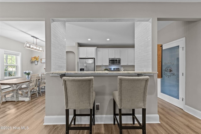 16 Starlit Ln, Pinehurst, NC 28374 - kitchen featuring appliances with stainless steel finishes, a kitchen breakfast bar, white cabinetry, light wood finished floors, and tasteful backsplash