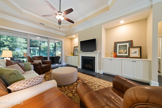 2675 Four Oak Rd, Southport, NC 28461 - living room with dark wood-style floors, a ceiling fan, a glass covered fireplace, ornamental molding, and a tray ceiling