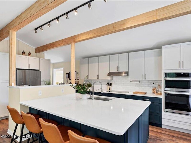 2670 Longleaf Dr SW, Pinehurst, NC 28374 - kitchen with stainless steel double oven, refrigerator, under cabinet range hood, black electric cooktop, and a kitchen bar