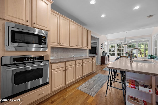 106 Blue Heron Cir, Sneads Ferry, NC 28460 - kitchen with appliances with stainless steel finishes, light brown cabinetry, light wood finished floors, a breakfast bar, and backsplash