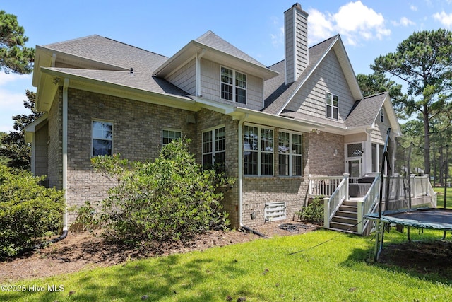 106 Blue Heron Cir, Sneads Ferry, NC 28460 - back of property with a trampoline, a lawn, a chimney, brick siding, and a shingled roof
