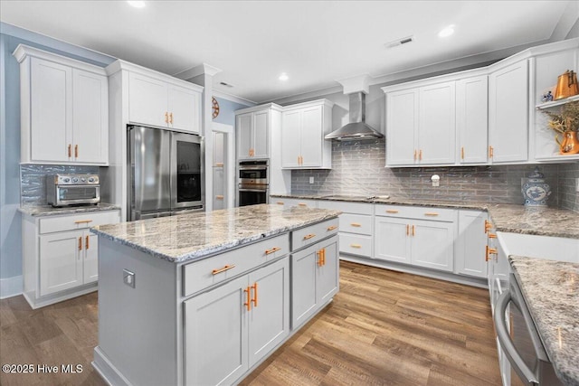 385 Summerhouse Dr, Holly Ridge, NC 28445 - kitchen featuring appliances with stainless steel finishes, wall chimney exhaust hood, a center island, light wood-style flooring, and white cabinets