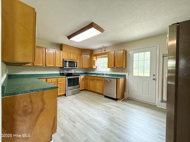 226 Community Rd, Lillington, NC 27546 - kitchen with stainless steel appliances, dark countertops, a textured ceiling, light wood-type flooring, and brown cabinetry