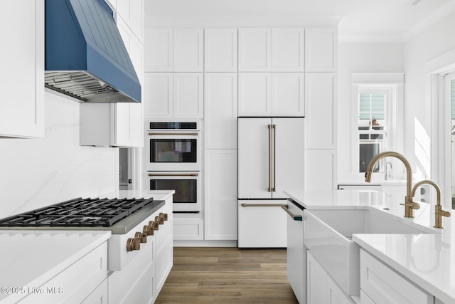 1320 Searay Ln, Carolina Beach, NC 28428 - kitchen with custom range hood, appliances with stainless steel finishes, white cabinetry, ornamental molding, and light wood-style flooring
