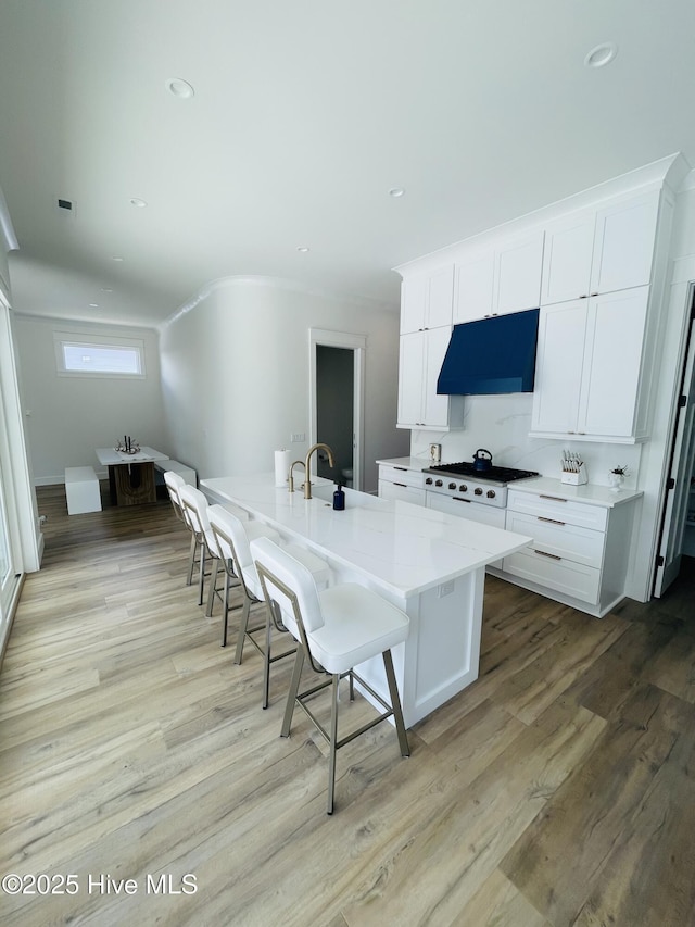 1320 Searay Ln, Carolina Beach, NC 28428 - kitchen with range hood, stovetop, a breakfast bar, white cabinets, and light wood finished floors