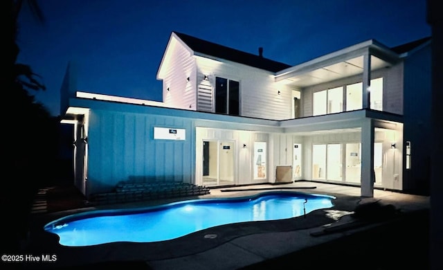 1320 Searay Ln, Carolina Beach, NC 28428 - back of house at night featuring board and batten siding, an outdoor pool, and a patio