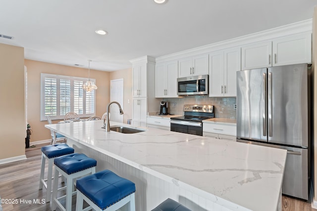 811 Colony Pl # D, Sunset Beach, NC 28468 - kitchen featuring appliances with stainless steel finishes, white cabinets, an island with sink, backsplash, and light wood finished floors