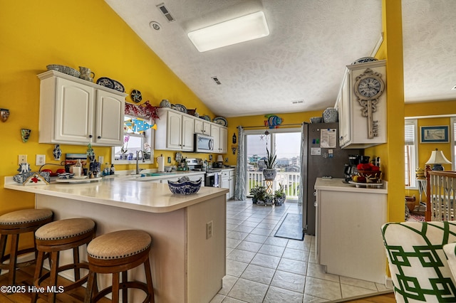 4061 4th St, Surf City, NC 28445 - kitchen featuring appliances with stainless steel finishes, a textured ceiling, lofted ceiling, a kitchen breakfast bar, and a peninsula