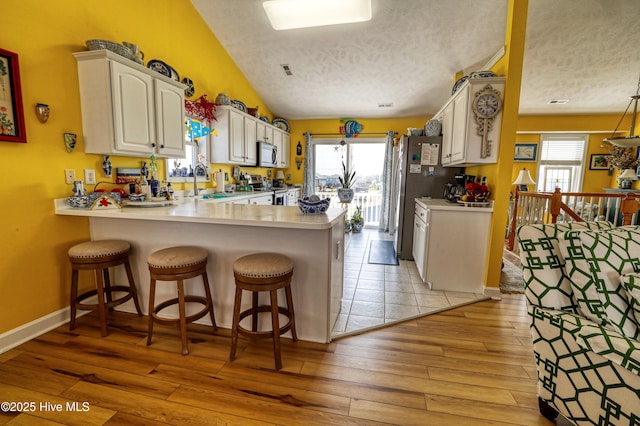 4061 4th St, Surf City, NC 28445 - kitchen with appliances with stainless steel finishes, a peninsula, a textured ceiling, light countertops, and a breakfast bar area