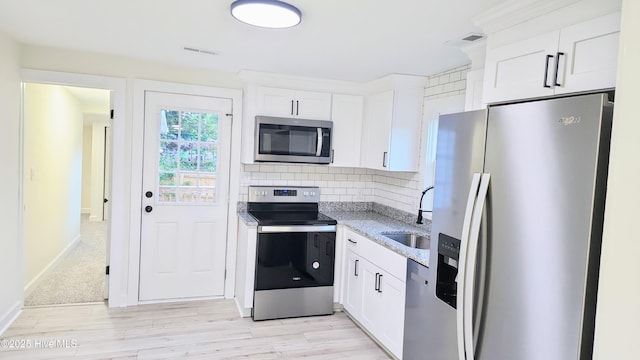 702A Richardson St # A, Elizabeth City, NC 27909 - kitchen featuring appliances with stainless steel finishes, light stone counters, white cabinets, decorative backsplash, and light wood-style flooring