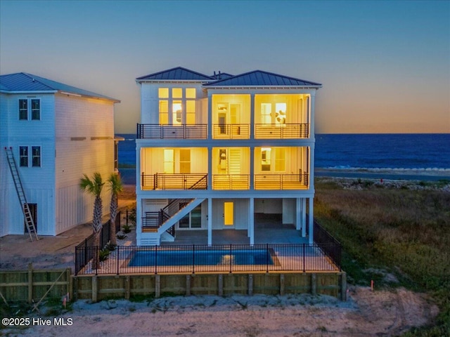 47 Grande View Dr, Ocean Isle Beach, NC 28469 - back of house at dusk with stairs, a balcony, a standing seam roof, a fenced backyard, and a patio