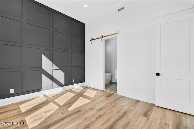 47 Grande View Dr, Ocean Isle Beach, NC 28469 - unfurnished bedroom featuring a decorative wall, light wood-type flooring, recessed lighting, a barn door, and ensuite bath