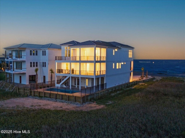 47 Grande View Dr, Ocean Isle Beach, NC 28469 - back of house at dusk featuring an outdoor pool, a water view, stairway, a standing seam roof, and a metal roof