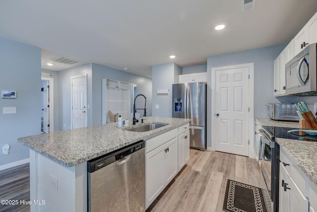 870 Westway Rd, Southport, NC 28461 - kitchen featuring appliances with stainless steel finishes, light wood-style floors, a center island with sink, white cabinets, and light stone countertops
