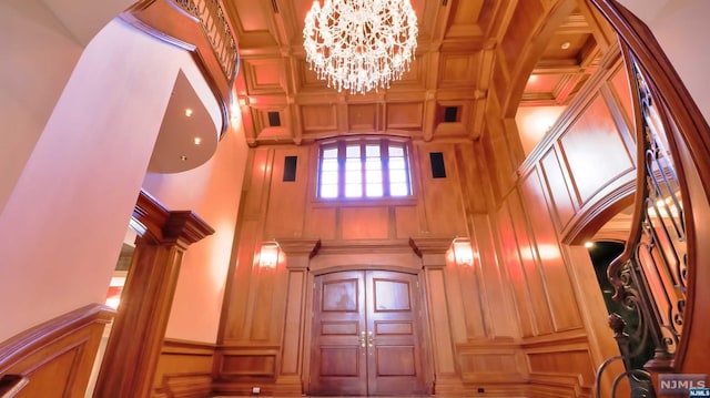 foyer entrance featuring a chandelier, a high ceiling, decorative columns, and wood walls