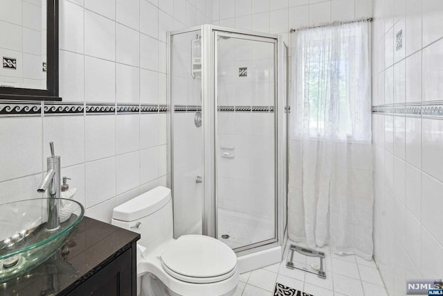 bathroom featuring tile patterned flooring, vanity, toilet, and tile walls