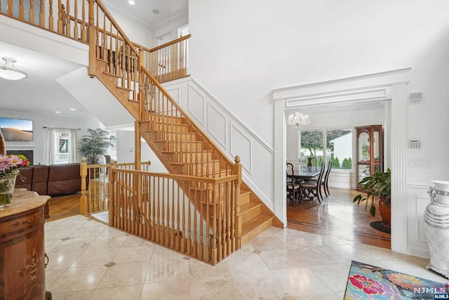 stairs with wood-type flooring, a towering ceiling, an inviting chandelier, and ornamental molding