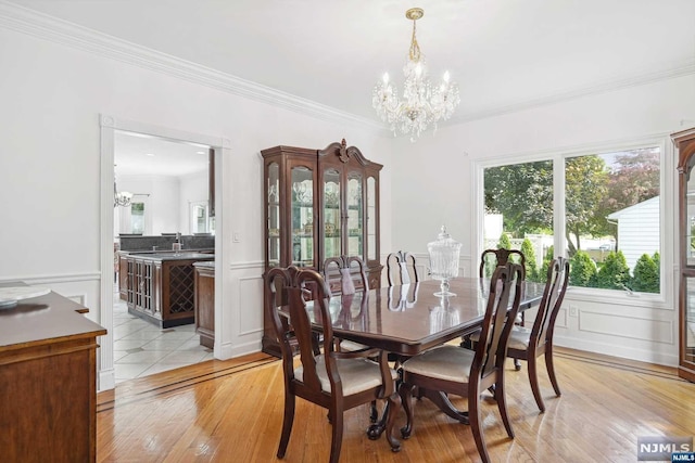 dining space with light hardwood / wood-style floors, ornamental molding, and a notable chandelier